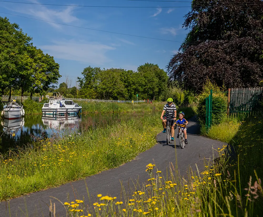 A family cycling beside a canal with boats floating on it